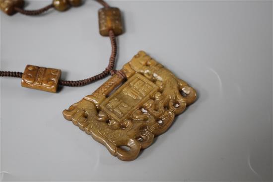 A Chinese hardstone necklace, with carved and inscribed plaque and brown fabric strung beads, plaque 6 x 4.5cm, rectangular beads 2cm a